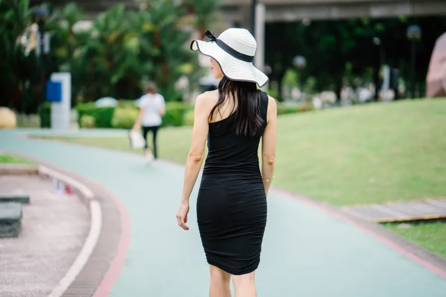 A person walking briskly along a curved park path on a bright day.